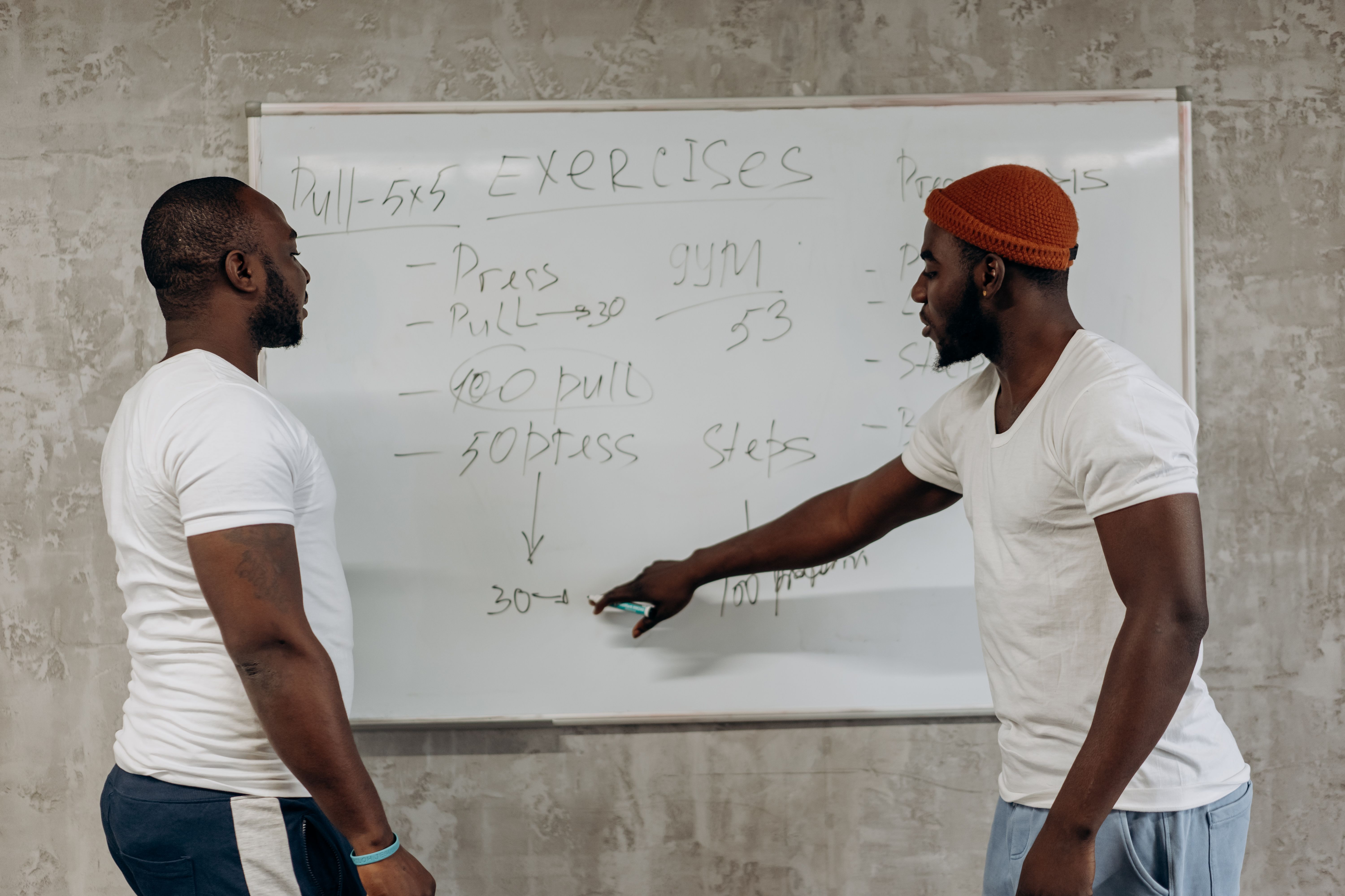 Dois homens conversando em frente a um quadro branco com um plano de exercícios escrito