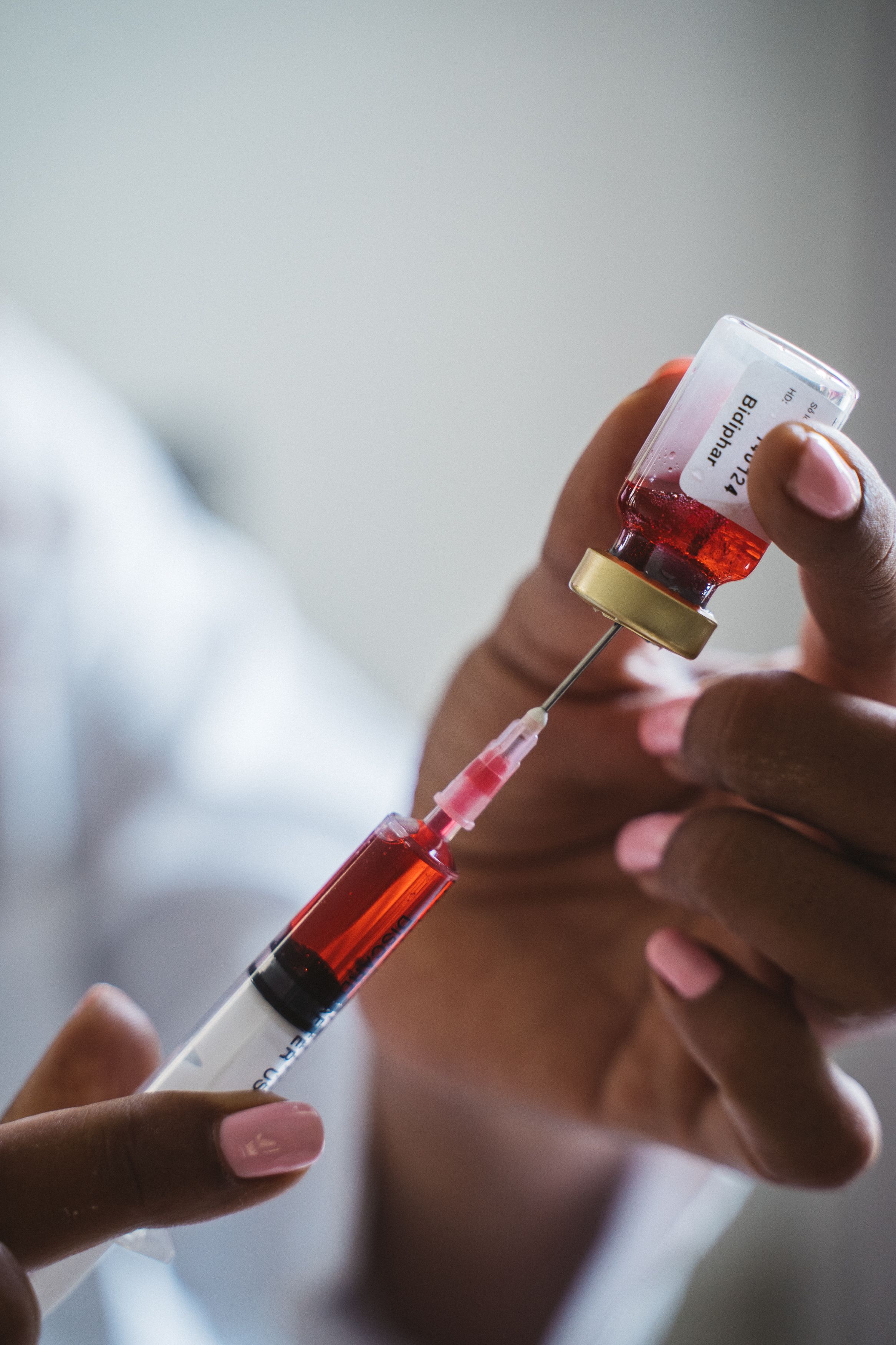 Mão segurando um frasco de medicamento vermelho enquanto enche uma seringa