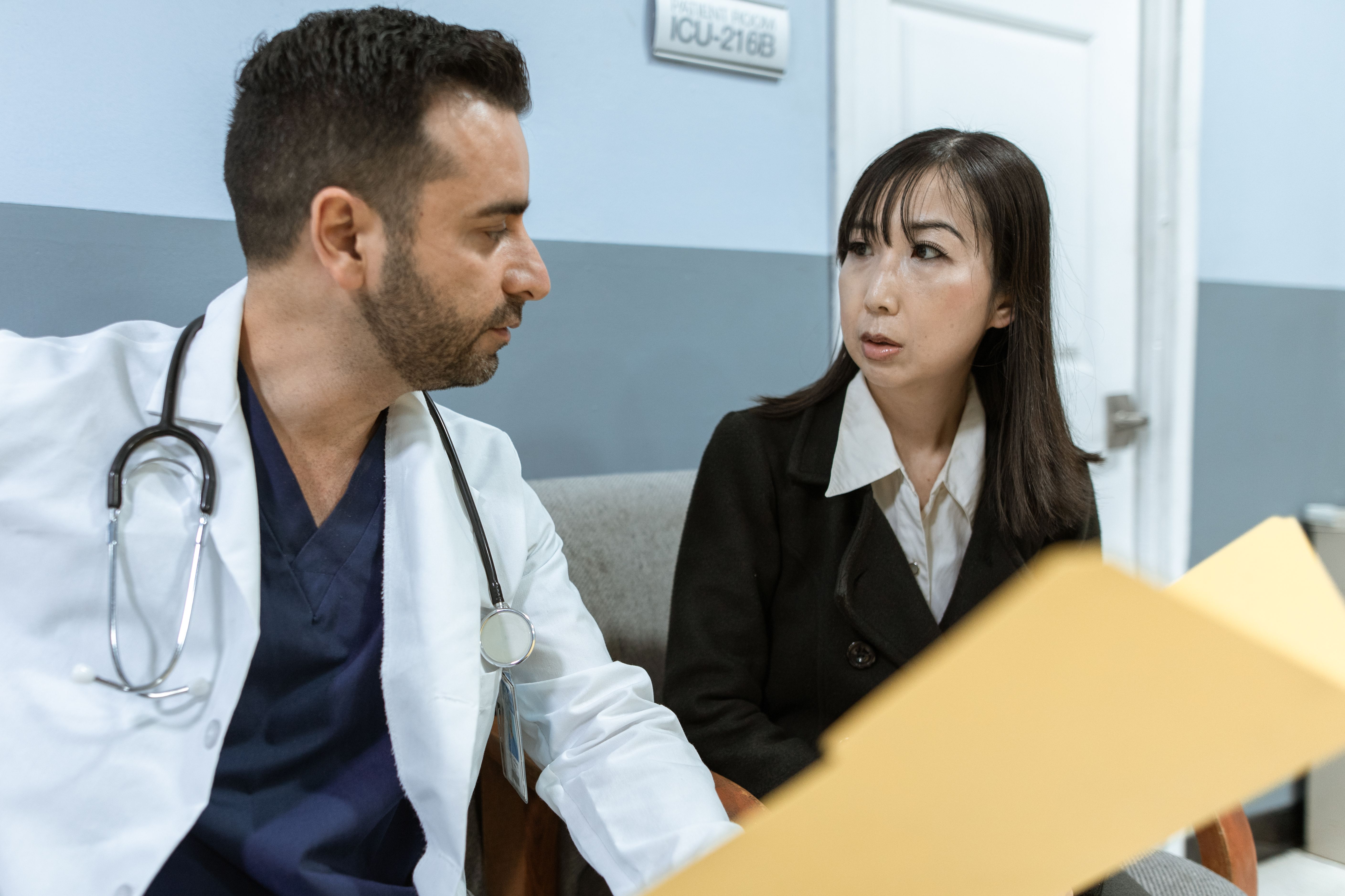 Médico conversando com uma paciente em um consultório, com uma prancheta em primeiro plano
