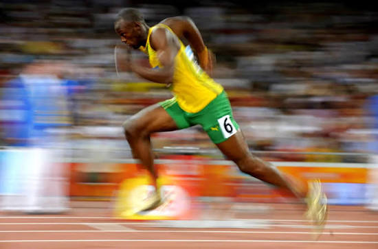 Velocista correndo os 100 metros com uniforme da Jamaica, em movimento borrado