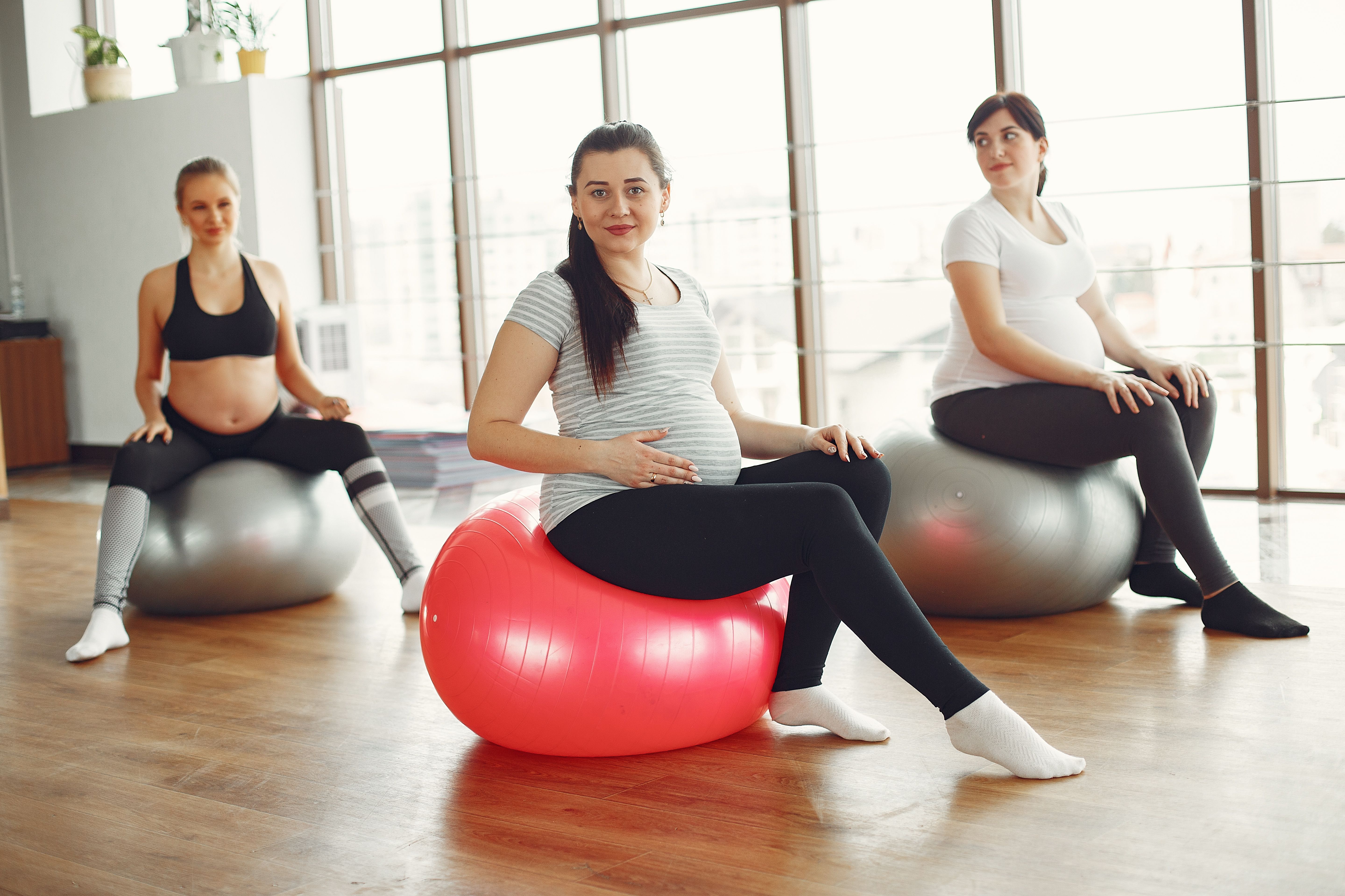 Três gestantes sentadas sobre bolas suíças durante uma aula de exercício