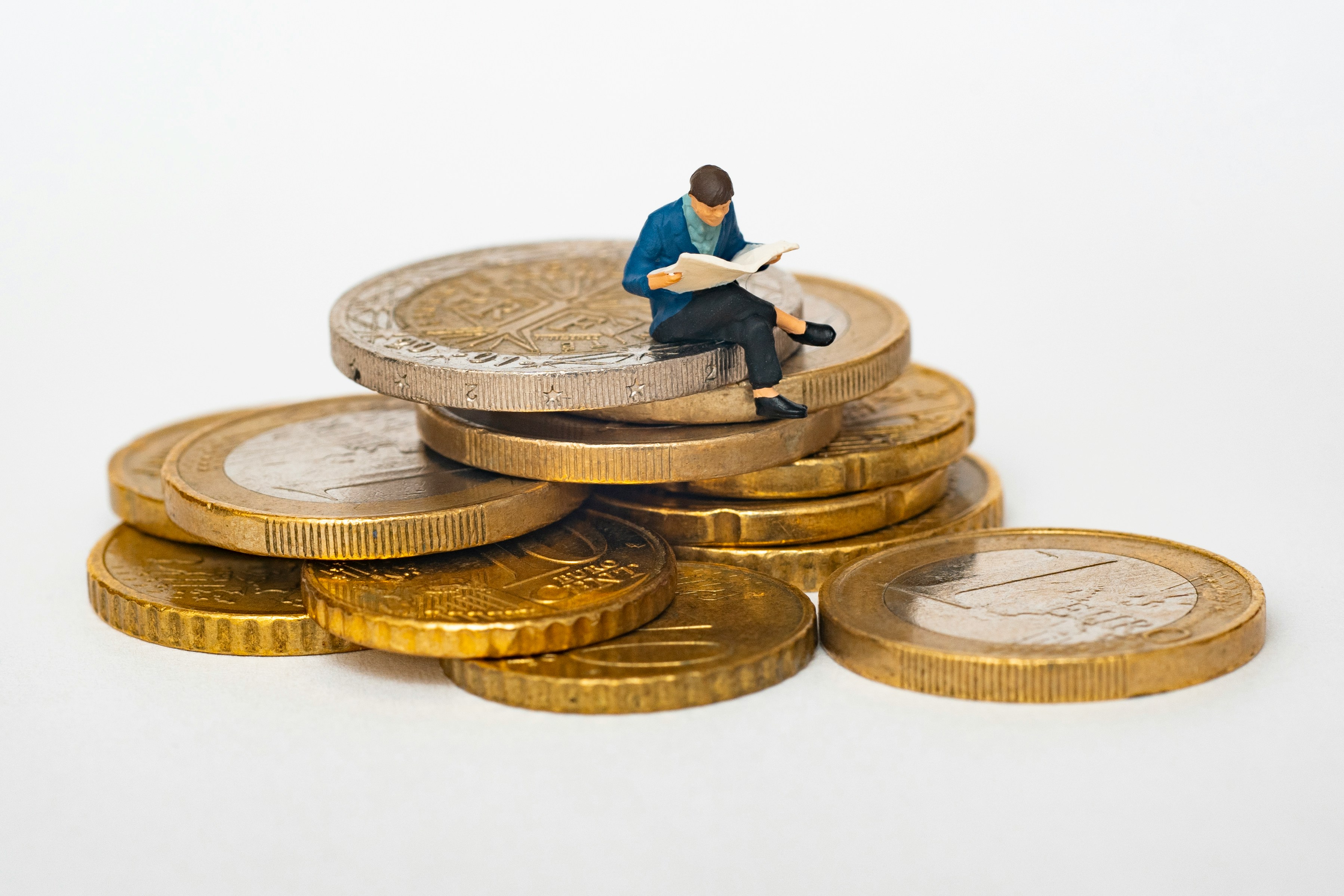 Miniatura de um homem lendo jornal, sentado sobre uma pilha de moedas de euro